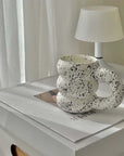 White speckled ceramic mug with a unique design on a table beside a white lamp.