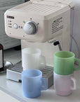 Pastel Muse Mugs in white, blue and green stacked beside an espresso machine