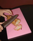 Slicing bread on the pink Strawberry Milk Puzzle Pop Chopping Board