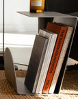 Bauhaus Steel Accent Table holding magazines in its slot, with a cup on top