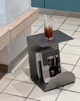 Bauhaus Steel Accent Table & Magazine Holder with a glass of iced coffee on a tiled floor