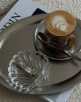 Matte Stainless Steel Oval Plate with a cappuccino, shell dish and magazine on a marble table