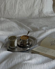 Matte Stainless Steel Oval Plate with a coffee cup and saucer on a white bed