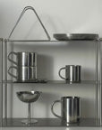 Aira Stainless Shelf, two-tier brushed steel riser holding steel cups and a tray