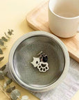 Kiyomi matcha sieve with cat charms on a wooden board beside a cup