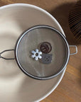 Kiyomi matcha sieve resting on a bowl with a flower charm