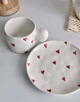 Ceramic mug and saucer set, decorated with red heart designs, featuring a 250ml capacity cup and matching plate on a white surface.