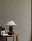 Elegant Hill Table Lamp with linen lampshade and ceramic base on a wooden side table, adding rustic charm to a modern living room.