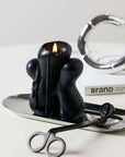 Black candle on stainless steel tray with wick trimmer, minimalist decor, modern home accessory display.