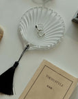Clear glass dish with rings on a white surface next to a book titled 'Tokyo Style'.