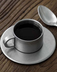 Stainless steel VINTAGE INOX cup and saucer on a wooden table, showcasing elegant design and durable materials.