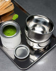 Spherical Cups on a steel tray with matcha powder and a bamboo whisk