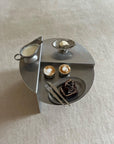 Modern round table set with stainless steel dishes, featuring two cappuccinos, a milk pitcher, cake slice, and whipped cream dessert.