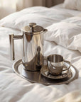 Silver coffee press and cup on a tray on a bed