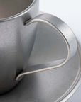 Close-up of a vintage inox stainless steel cup with a handle and matching saucer, showcasing elegant craftsmanship and design.