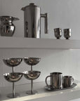 Stainless steel kitchenware set including mugs, cups, and a teapot with a sleek modern design on display shelves