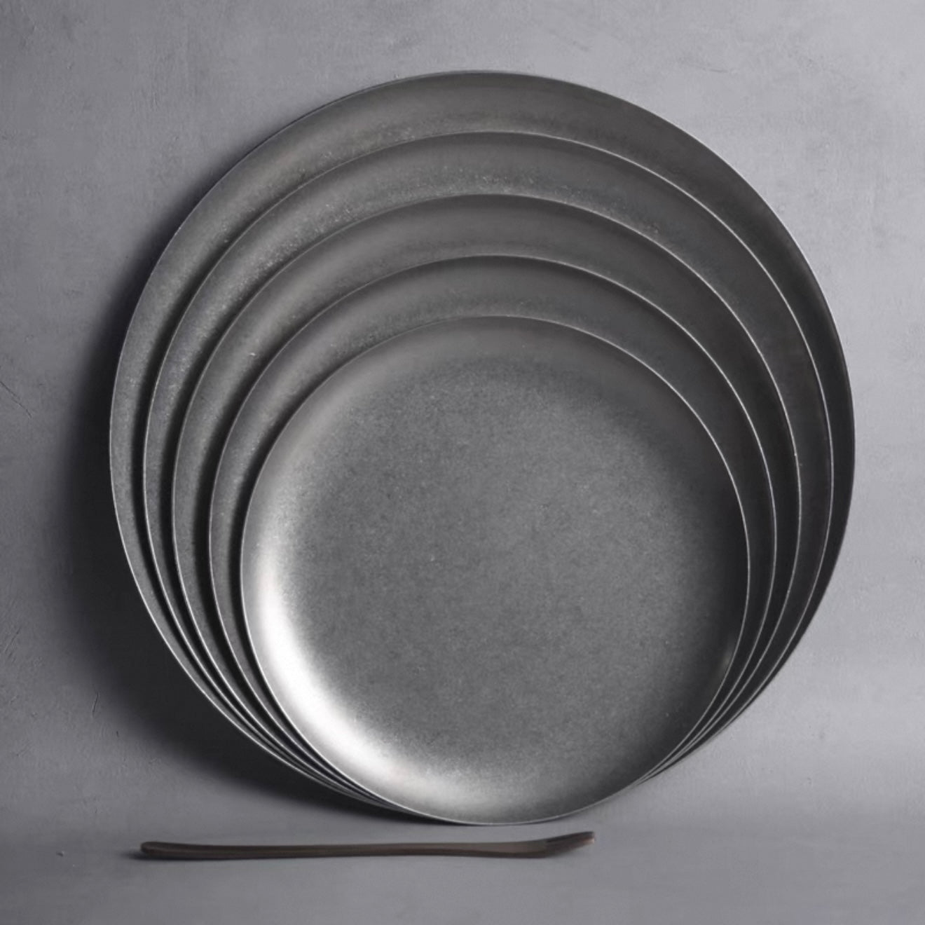 Stack of Hakone Plates in matte-finished stainless steel, showcasing minimalist design and elegant curves for dining.