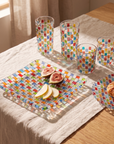Tessera Table set, square: square platter with figs, 23.5 cm plate with a pastry and four mosaic glasses on a linen-covered table