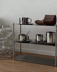 Aira Stainless Shelf displaying steel cups and a glass pitcher in a living room
