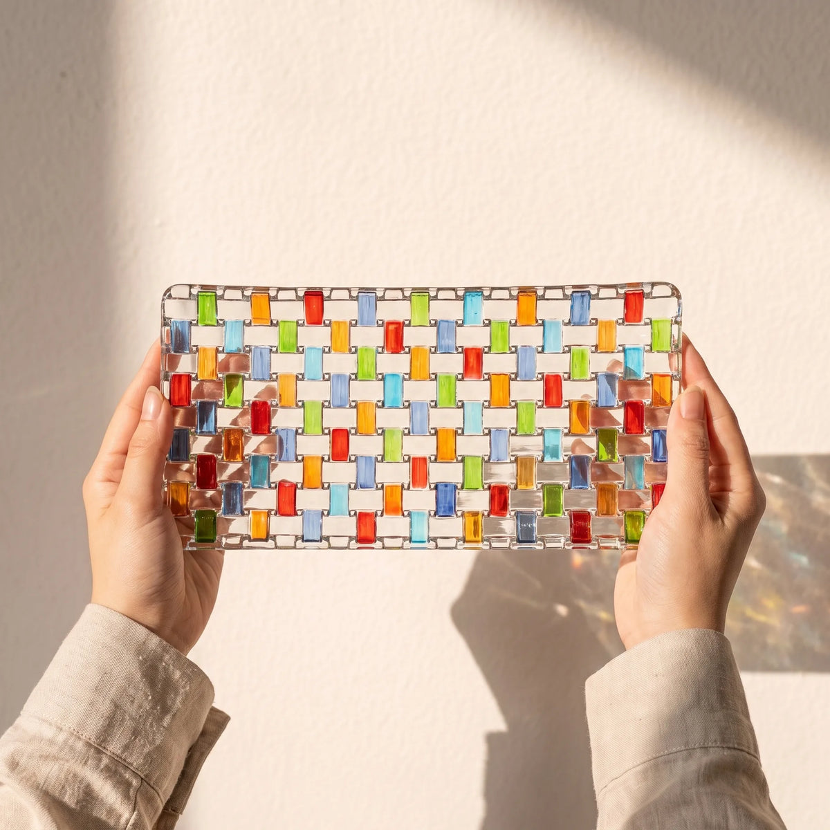 Hands holding the Tessera hand-painted rectangular platter against a sunlit wall