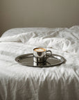 Matte Stainless Steel Oval Plate with a steel coffee cup on a white bed