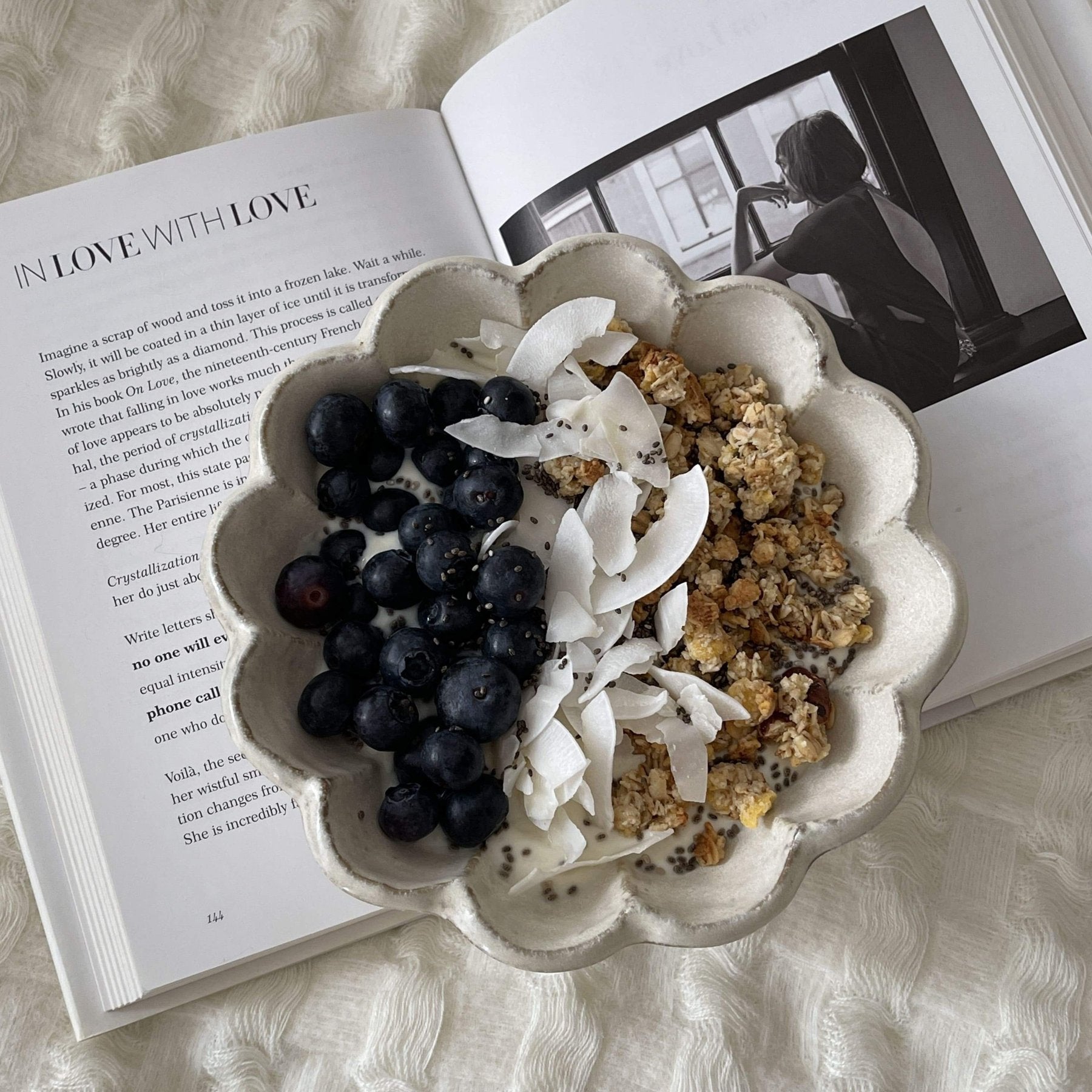 Rinka porcelain bowl with blueberries, coconut flakes, and granola on an open book background.