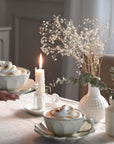 Elegant afternoon tea set with soup cups and plates, featuring a serene candlelit setting and decorative dried flowers.