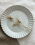 Marumitsu Barbarie plate with petal-like rim and dried flowers on neutral cloth background.