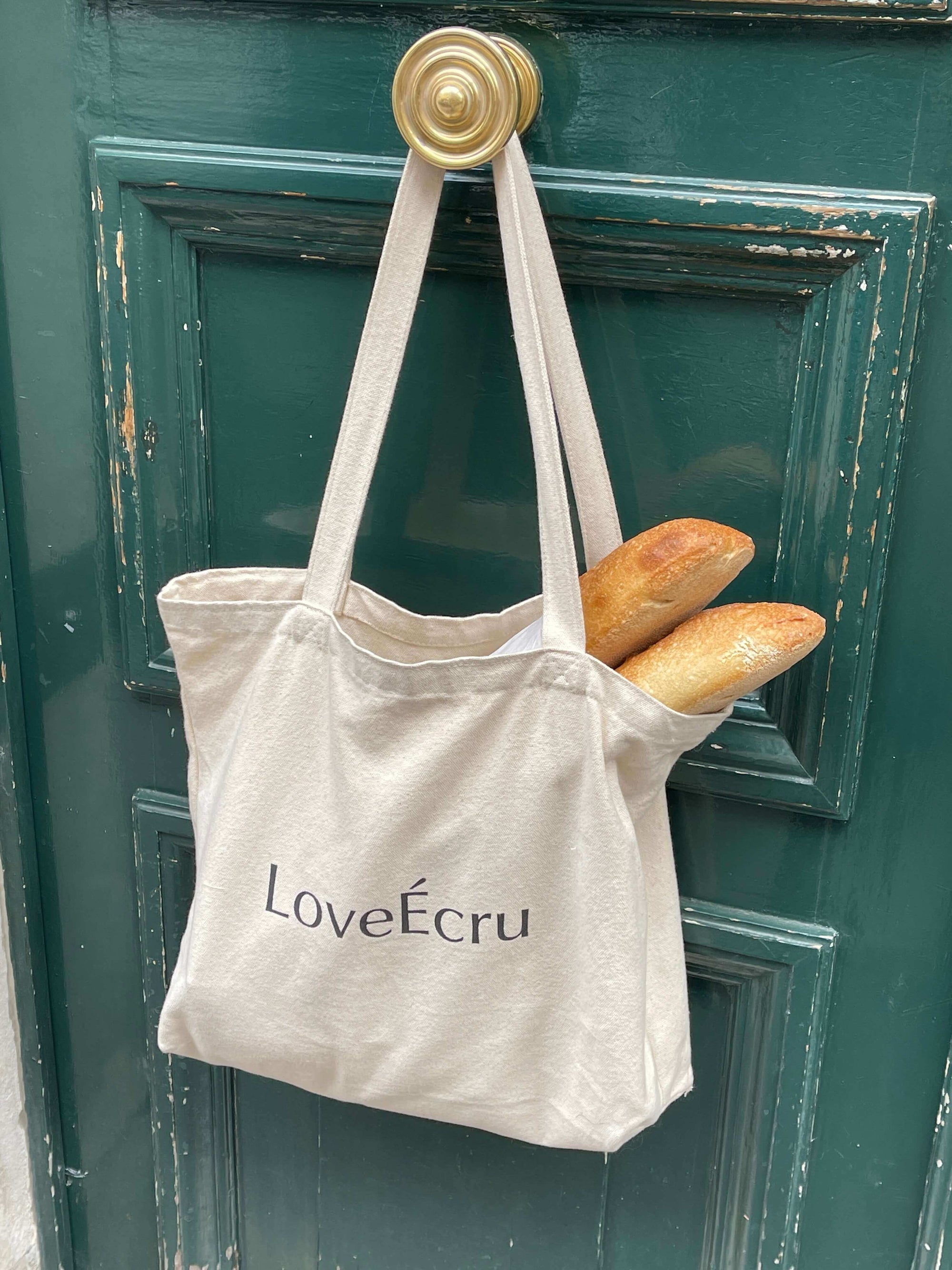 Canvas tote bag with baguettes hanging on a green door handle.