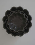 Stack of Rinka bowls in black porcelain, featuring floral shapes from the Kaneko Kohyo collection, showcasing Japanese craftsmanship.