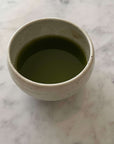 Ivory Matcha Bowl filled with green matcha tea, showcasing its rounded form and calm colors, made of Mino ware porcelain.