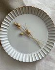 Marumitsu Barbarie plate with petal-like rim and dried flowers on a fabric background