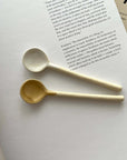 Two Marumitsu Bean Spoons on a book, showcasing their unique bean-shaped tips and rustic glaze finish.