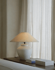 Pot lamp with linen shade on wooden table, enhancing room decor with adjustable light, creating a quiet and comfortable atmosphere.