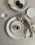 Elegant porcelain plates with figs, showcasing nostalgic lace edge design, atop a neutral linen tablecloth for a sophisticated dining setting.