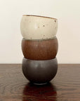 Stack of three Rila Tea Cups with textured surfaces in warm matte colors on a wooden table.
