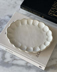 Rinka Oval Plate made of delicate porcelain with a flower shape, resting on books, part of the Kaneko Kohyo Rinka Collection.