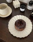 Elegant white Rinka Plate by Yoshida Pottery holding a chocolate dessert, styled with candles and a textured mug on a wooden table.