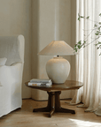 Egg-shaped clay pot table lamp with linen shade on a wooden table beside a white sofa, creating a peaceful room ambiance.