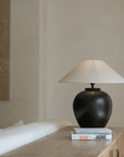 Egg-shaped clay pot table lamp with linen shade on a wooden table setting a peaceful ambiance in a cozy room.