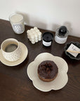Elegant table setting with a coffee cup and a chocolate pastry on a unique flower-shaped plate, surrounded by candles and decor.