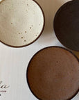 Three Rila 16cm porcelain plates with matte texture by Kaneko Kohyo, showcasing warm colors, perfect for relaxation. Made in Japan.