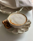 Rinka porcelain cup with frothy coffee on flower-shaped plate by Kaneko Kohyo, showcasing elegant white design and delicate craftsmanship.