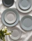 Elegant porcelain plates with soft lace edges and flecked lacquer finish, displayed on a white cloth with flowers.